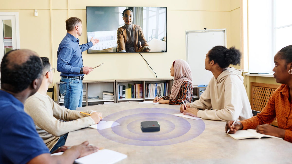 A training session in a classroom, students around the table and a remote participant on the wall screen